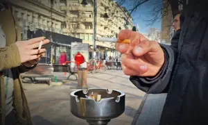 Dwie osoby palą papierosy na ulicy. W tle widać budynki i ludzi. Ceny papierosów w Albanii mogą być różne.