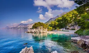 Malownicza brela plaża z krystalicznie czystą wodą, skalistymi zatoczkami i górami w tle.