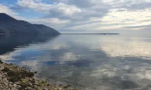 Spokojne morze w Czarnogórze we wrześniu. Góry w oddali, chmury odbijające się w wodzie.