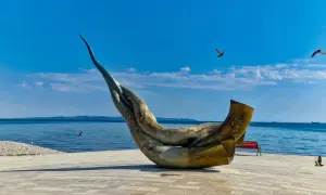 Monumentalna rzeźba na promenadzie w Durrës, plaża w tle, błękitne niebo i morze.