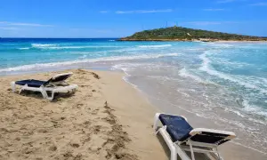Plaża na Cyprze zimą. Dwa puste leżaki na piasku, turkusowe morze i zielone wzgórze w oddali.