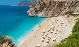 Malownicza plaża w Turcji z turkusową wodą i skalistymi klifami. Rzędy leżaków i parasoli zapraszają do odpoczynku.