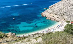 Rajska plaża w Baška Chorwacja, z turkusową wodą, łodziami i mnóstwem plażowiczów.