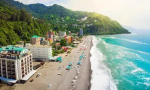 Widok na plażę i hotele w Batumi, Gruzja. Zielone wzgórza schodzą do turkusowego morza, a na kamienistej plaży widać parasole i leżaki.