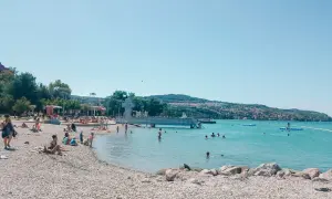 Słoneczna Słowenia zachwyca plażami. Ludzie kąpią się i opalają na kamienistym brzegu, ciesząc się błękitem Adriatyku.