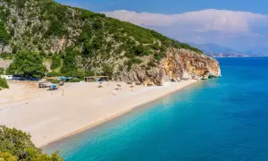 Piękna plaża Dhermi z turkusową wodą, skalistym klifem i zielonymi wzgórzami.