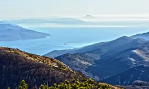 Widok z Učka Nature Park na zatokę z kontenerowcem. Góry w odcieniach niebieskiego i zieleni.