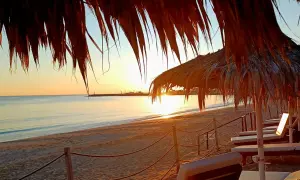Zachód słońca na plaży w Ayia Napa. Leżaki pod słomianymi parasolami czekają na turystów. Idealne miejsce, by zobaczyć piękno Cypru.