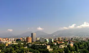 Widok na miasto z górami w tle. Widać nowoczesne budynki i zieleń. Idealne miejsce na **Albania roaming** i odkrywanie krajobrazów.