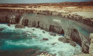 Wysokie klify i turkusowe morze przy Cape Greco na Cyprze. Fale rozbijają się o skały.