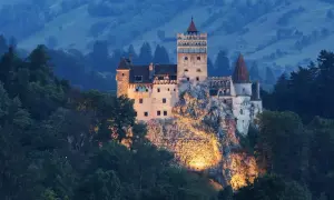 Zamek Bran w Transylwanii, oświetlony nocą, na tle zalesionych wzgórz.