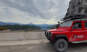 Czerwony Land Rover na tle gór i jeziora. Chłodna, pochmurna pogoda, typowa dla Albanii w styczniu.