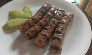 Grillowane kiełbaski na talerzu z plasterkami ogórka. Idealne danie, by dowiedzieć się, co zjesc w Bułgarii.