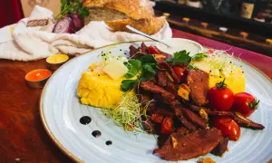 Pyszne jedzenie w Rumunii: polenta z wołowiną, pomidorkami i serem. Obok świeży chleb i świece tworzą przytulną atmosferę.