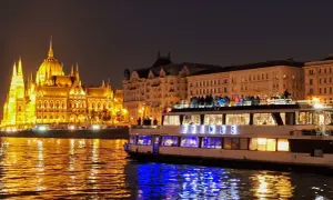 Nocny rejs po Dunaju w Budapeszcie. Oświetlony Parlament i statek z pasażerami na pokładzie odbijają się w wodzie.