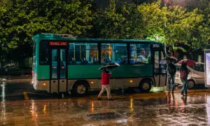 Deszczowa noc w Tiranie. Ludzie z parasolami czekają na autobus do Durrës.