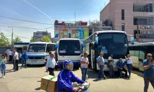 Autobusy na dworcu, jeden z nich jedzie do Vlory, inny do Tirany. Ludzie czekają na podróż.
