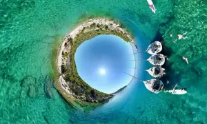 Rajskie **peloponez plaże** z krystalicznie czystą wodą, żaglówkami i ludźmi kąpiącymi się w słońcu.