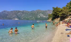Słoneczny dzień na Perast beach. Ludzie kąpią się w krystalicznie czystej wodzie, podczas gdy góry w tle tworzą malowniczy krajobraz.