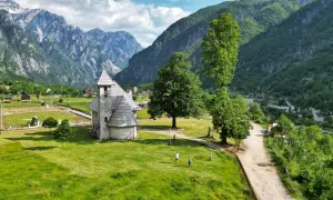 Kamienna cerkiew w Theth, Albania, otoczona zielonymi wzgórzami i majestatycznymi górami.