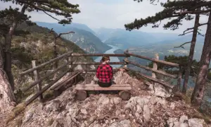 Widok na rzekę z punktu widokowego w Serbii. Kobieta w kratę siedzi na ławce, podziwiając krajobraz. Serbia atrakcje.