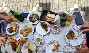 Stół zastawiony pysznym jedzeniem, typowym dla Albanii. Widać dania mięsne, gołąbki, pieczywo, kawę i piwo.