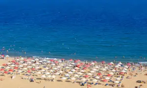 Słoneczny brzeg tętni życiem. Tłumy plażowiczów odpoczywają pod parasolami, kąpią się w morzu i opalają na piasku.