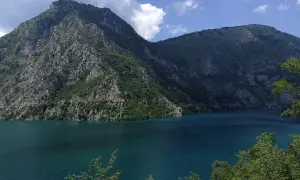 Piękne, turkusowe Pivsko Jezero otoczone skalistymi górami porośniętymi zielenią.