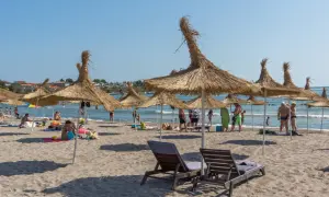 Słoneczna plaża z parasolami z trawy, leżakami i ludźmi cieszącymi się wakacjami. To idealne miejsce na **carewo atrakcje**.