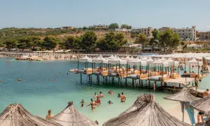 Słoneczne **ksamil dzikie plaże** z turkusową wodą, drewnianymi pomostami z leżakami i mnóstwem wypoczywających ludzi.