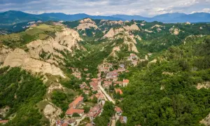Malowniczy widok na Melnik w Bułgarii, z domami z czerwonymi dachami wciśniętymi między zielone wzgórza i skalne formacje.