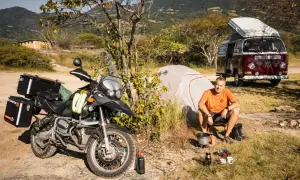Motocykl, namiot i kamper to idealny zestaw, by wiedzieć, co zabrać na camping. Mężczyzna gotuje na kuchence turystycznej.