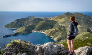 Widok na zatokę i górzysty krajobraz przylądka Matapan. Kobieta z plecakiem podziwia panoramę.