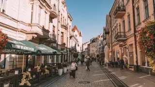 Spacer po urokliwym rynku w Nowym Sączu. Brukowana uliczka, kamienice, ogródki kawiarniane i ludzie spacerujący w słoneczny dzień.