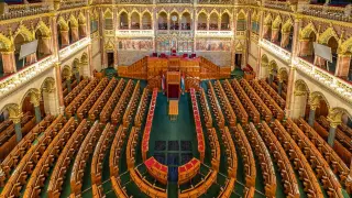 Wnętrze parlamentu w Budapeszcie, pełne rzędów drewnianych ławek i bogatych zdobień, czeka na debatę.