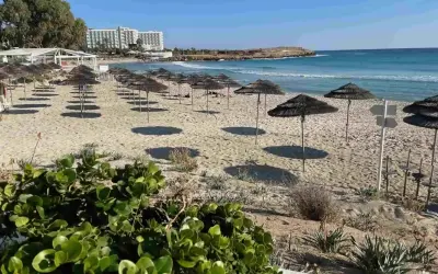 Puste cypr plaże z rzędami parasoli i hotel w tle. Słońce rzuca długie cienie na piasek.