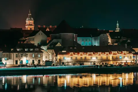 Nocny widok na zabytkowe budynki w Mariborze, Słowenia, z odbiciami świateł w rzece.