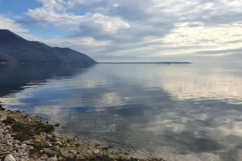 Spokojne morze w Czarnogórze we wrześniu. Góry w oddali, chmury odbijające się w wodzie.