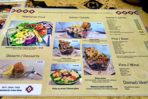 Menu z kuchnią bośniacką: wegetariański talerz, sałatki (w tym szopska), desery, piwo i wino.
