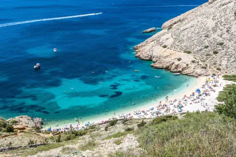 Rajska plaża w Baška Chorwacja, z turkusową wodą, łodziami i mnóstwem plażowiczów.