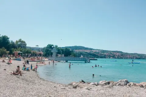 Słoneczna Słowenia zachwyca plażami. Ludzie kąpią się i opalają na kamienistym brzegu, ciesząc się błękitem Adriatyku.