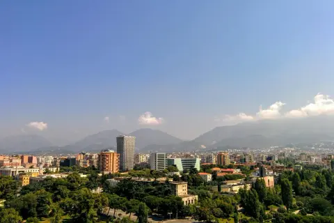 Widok na miasto z górami w tle. Widać nowoczesne budynki i zieleń. Idealne miejsce na **Albania roaming** i odkrywanie krajobrazów.