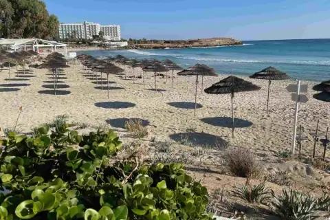 Puste cypr plaże z rzędami parasoli i hotel w tle. Słońce rzuca długie cienie na piasek.