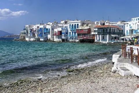 Malownicze Mykonos: białe domy z niebieskimi okiennicami nad turkusowym morzem. Warto sprawdzić mykonos ceny przed podróżą.