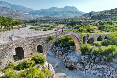 Kamienna, zabytkowa konstrukcja w Szkodrze, Albania, z kobietą w fioletowej sukni na szczycie.