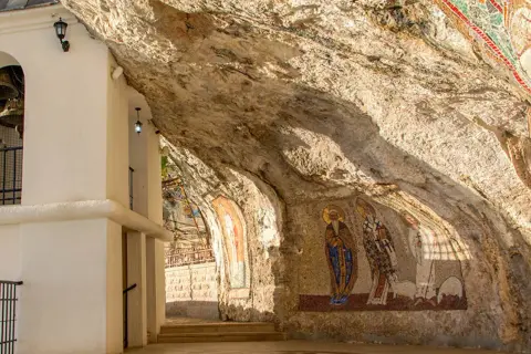 W skalnych niszach monasteru Ostrog widnieją mozaiki świętych. Biała architektura kontrastuje z surową skałą.