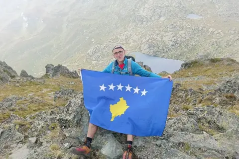 Mężczyzna z flagą Kosowa na szczycie góry. Niesamowite kosowo wakacje w górach.