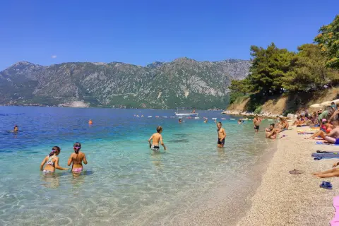 Słoneczny dzień na Perast beach. Ludzie kąpią się w krystalicznie czystej wodzie, podczas gdy góry w tle tworzą malowniczy krajobraz.