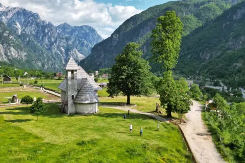 Kamienna cerkiew w Theth, Albania, otoczona zielonymi wzgórzami i majestatycznymi górami.