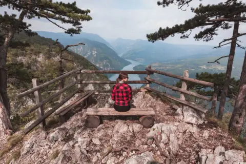 Widok na rzekę z punktu widokowego w Serbii. Kobieta w kratę siedzi na ławce, podziwiając krajobraz. Serbia atrakcje.